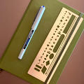 A pen and short metal ruler sitting on top of a sage Luechterm917 dotted notebook.
