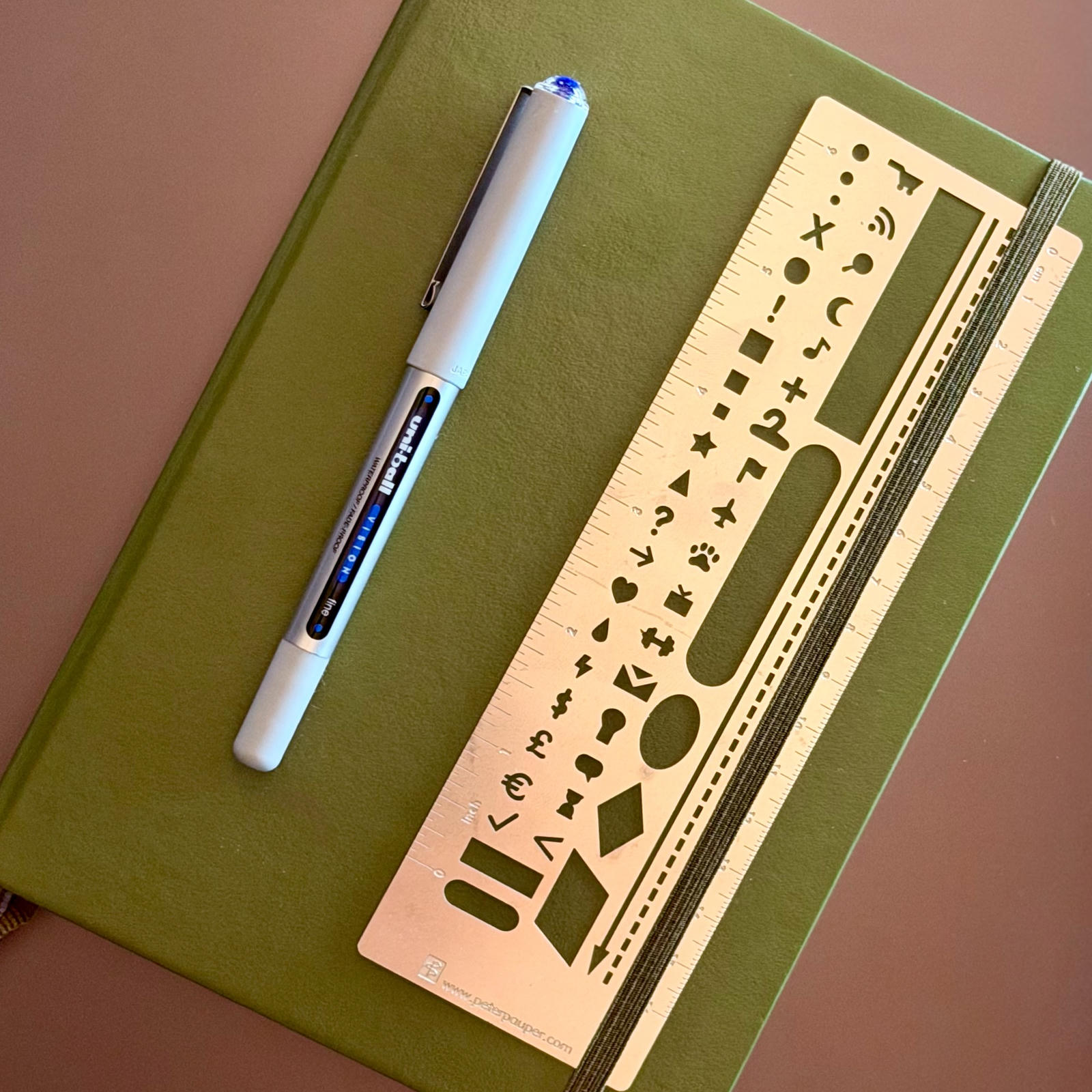A pen and short metal ruler sitting on top of a sage Luechterm917 dotted notebook.
